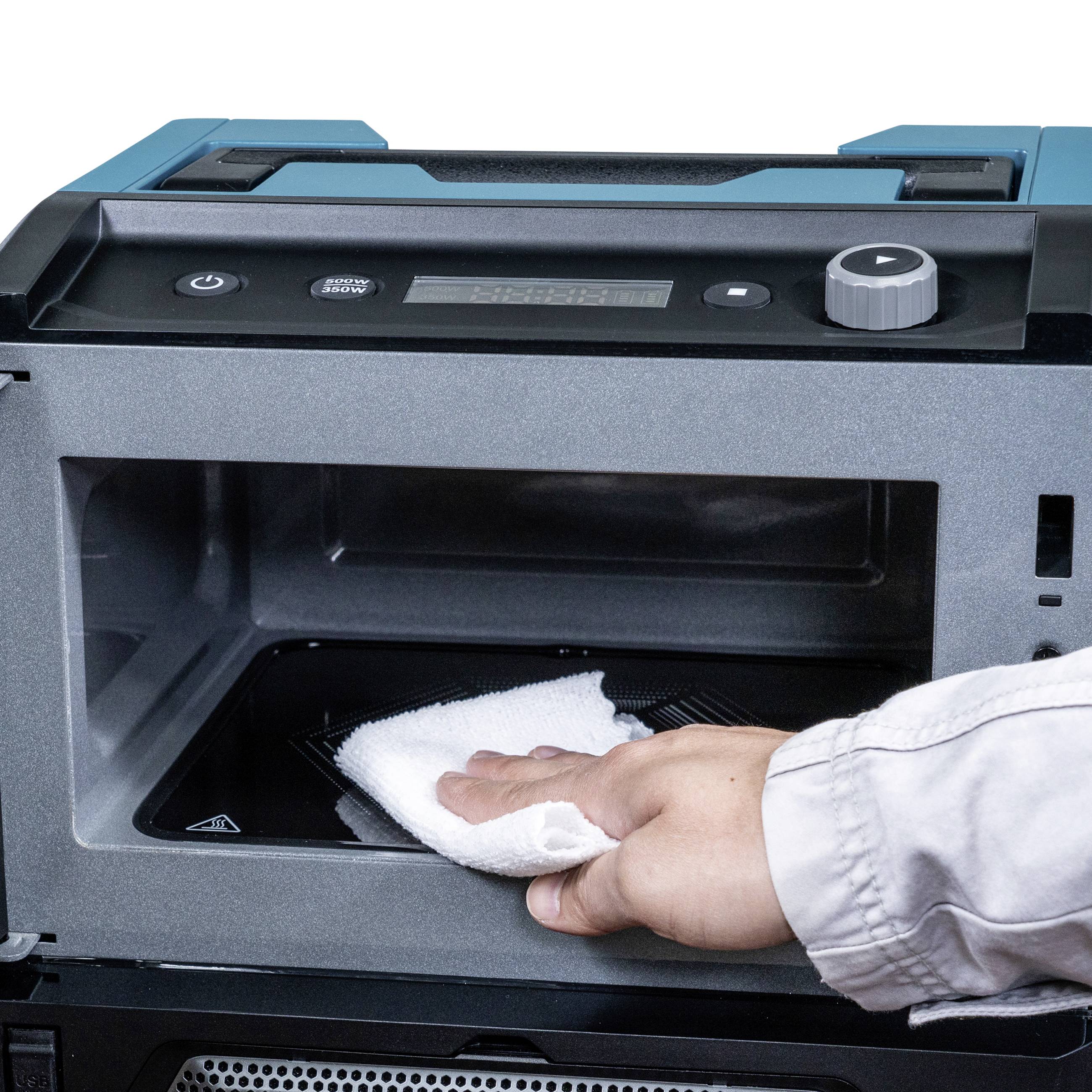 A hand is wiping the interior of a microwave oven clean with a cloth. The appliance is open and being cleaned.