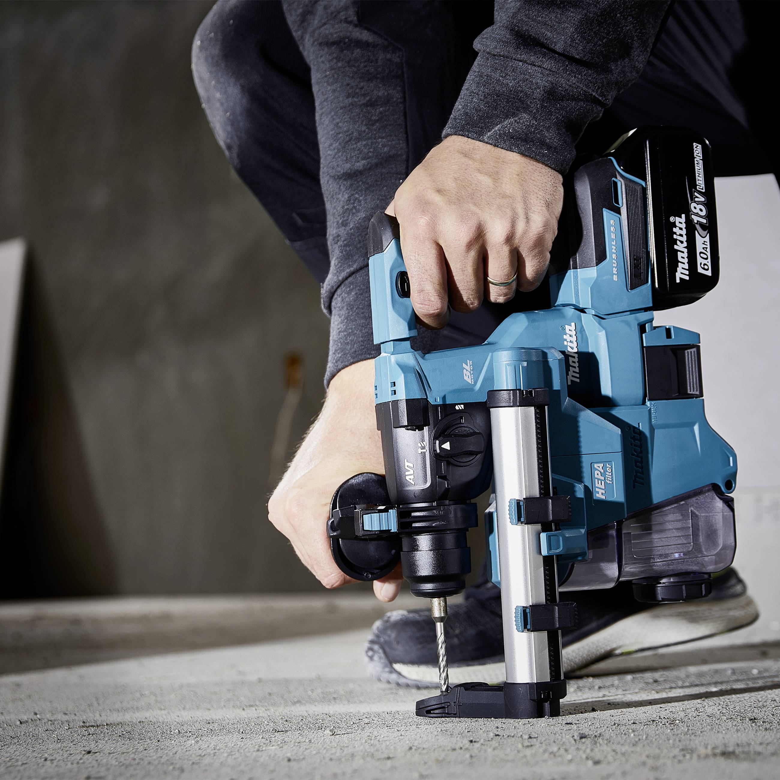 A person is drilling a hole with a blue, battery-powered drill hammer on a concrete surface. Background: blurred wall.
