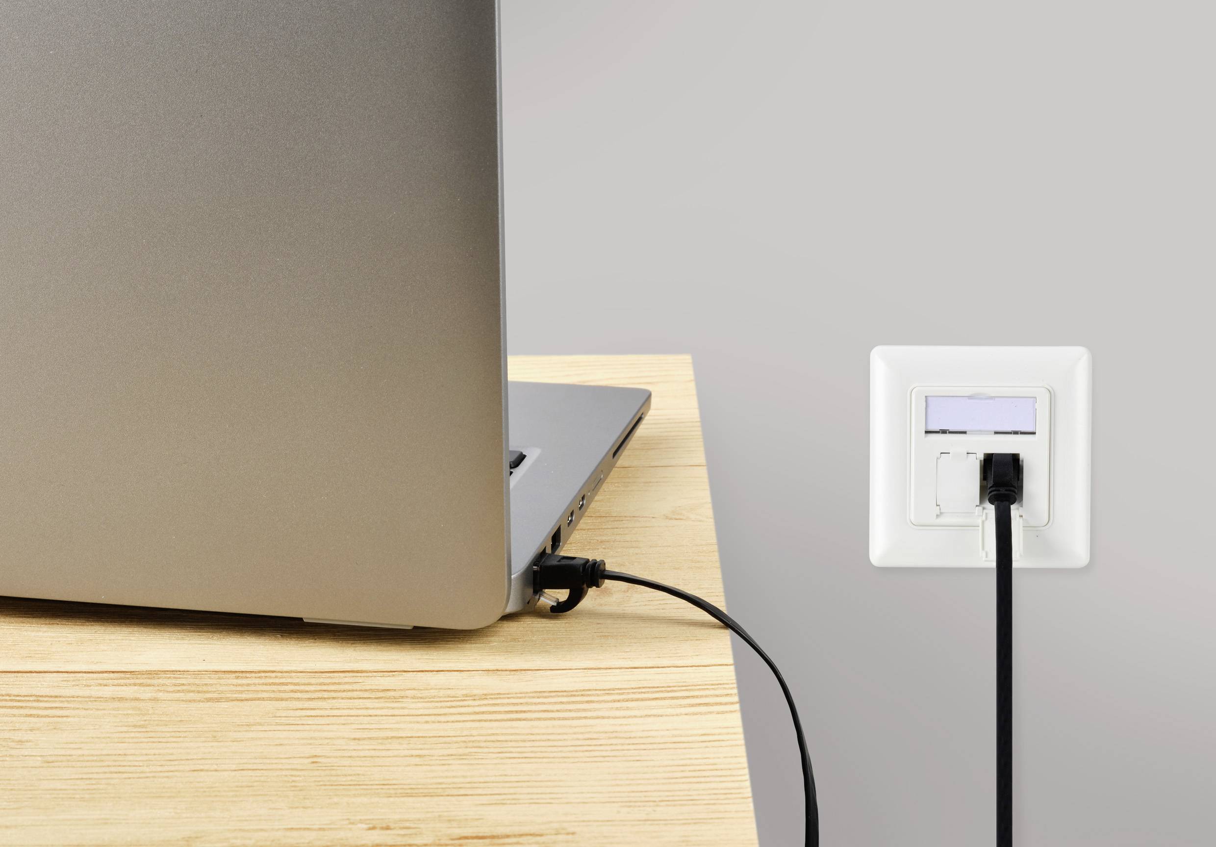 A laptop is connected to a wall socket via a black cable on a wooden table.