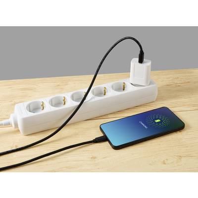 A mobile phone is lying on a table and being charged via a cable connected to a power strip. The display reads 'Charging'.