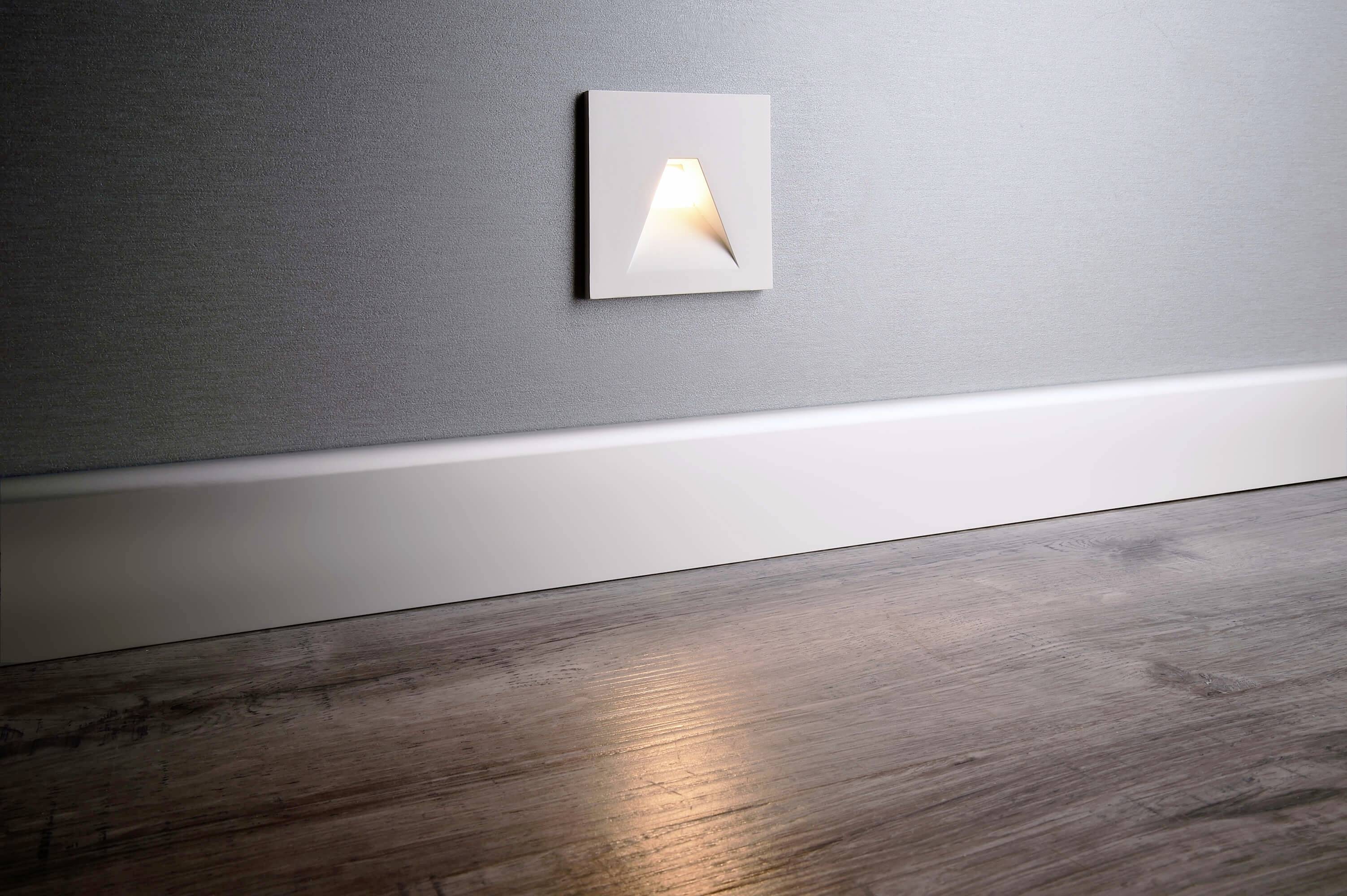 Illuminated wall switch in modern interior design, with wooden flooring and white skirting board. Switch emits a warm light.