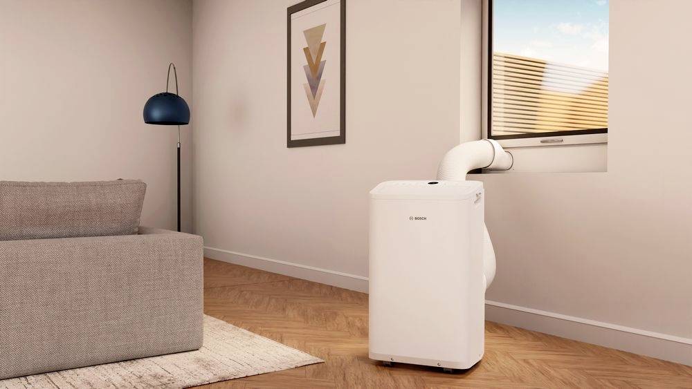 A portable air conditioning unit is connected to a window in a modern living room. Beside it stands a blue and white lampshade.