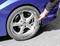 A person is tightening a wheel nut with a spanner on a blue car. The car is parked on an asphalt surface.