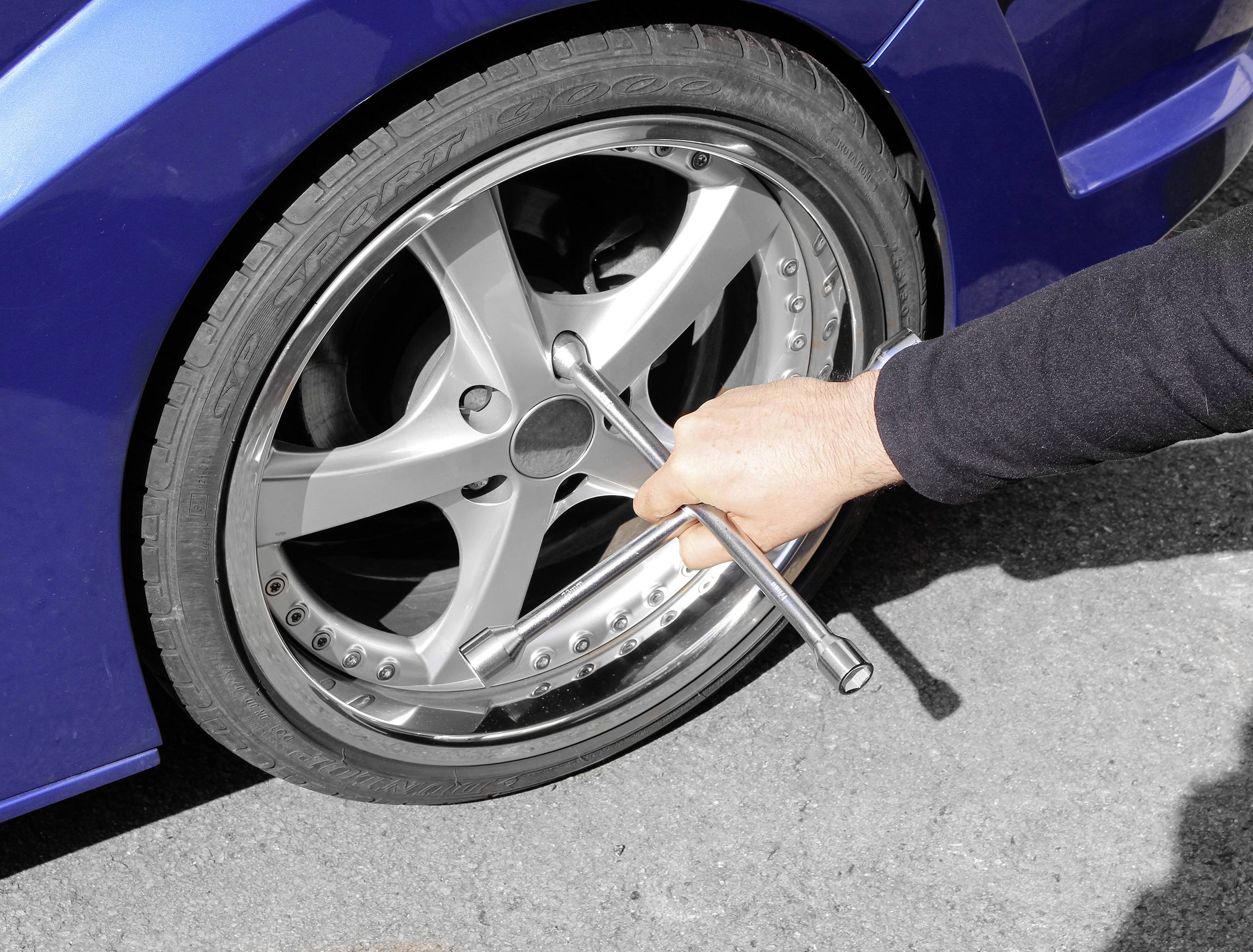A person is changing a car tyre and tightening the wheel nuts with a cross spanner. The car has a blue bodywork.