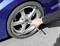 A person is changing a car tyre and tightening the wheel nuts with a cross spanner. The car has a blue bodywork.