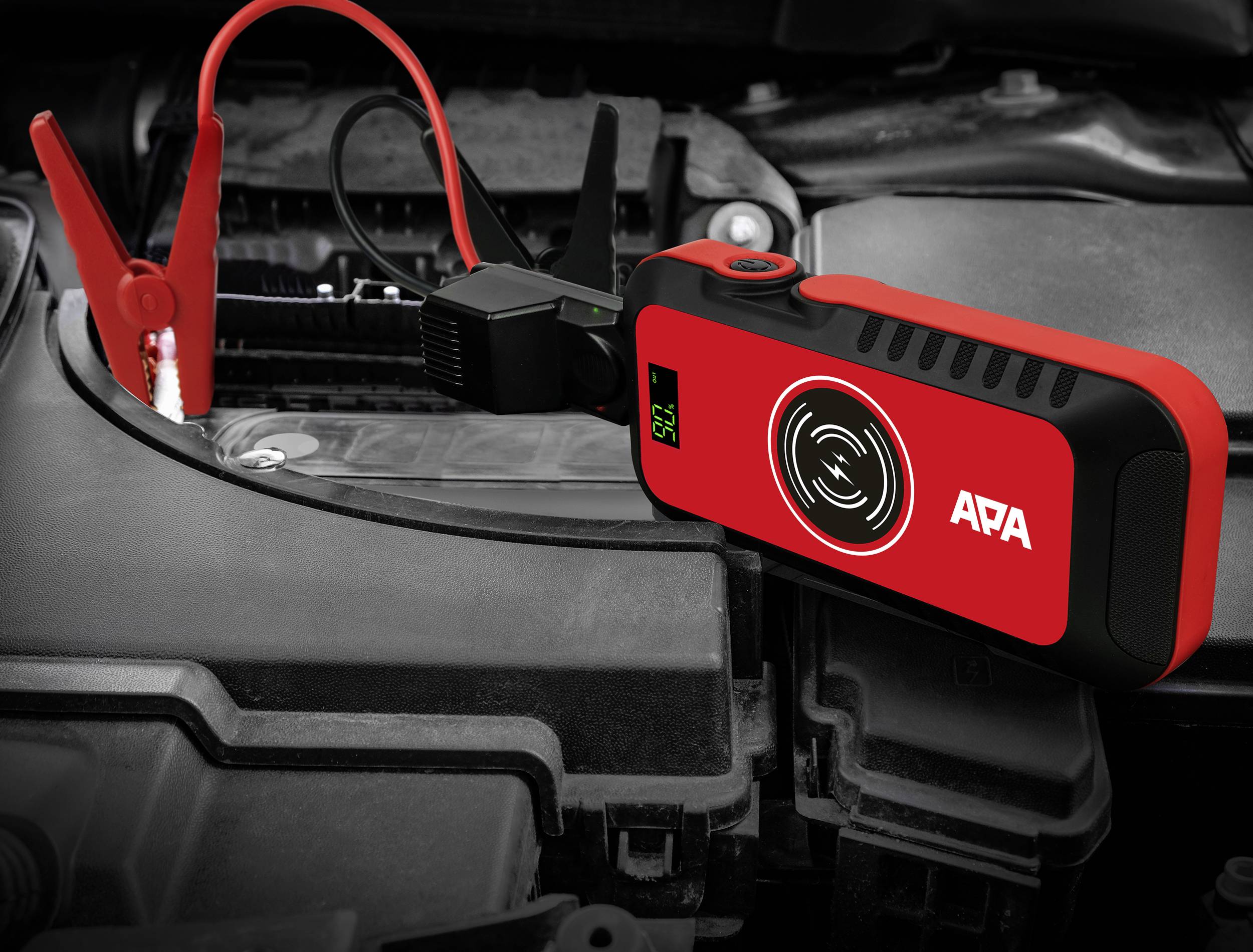Compact red car battery jump starter in use beneath a car bonnet, connected to car battery terminals.