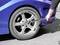 A person is changing the tyre of a blue car with a tool. The focus is on the car tyre and the tool.