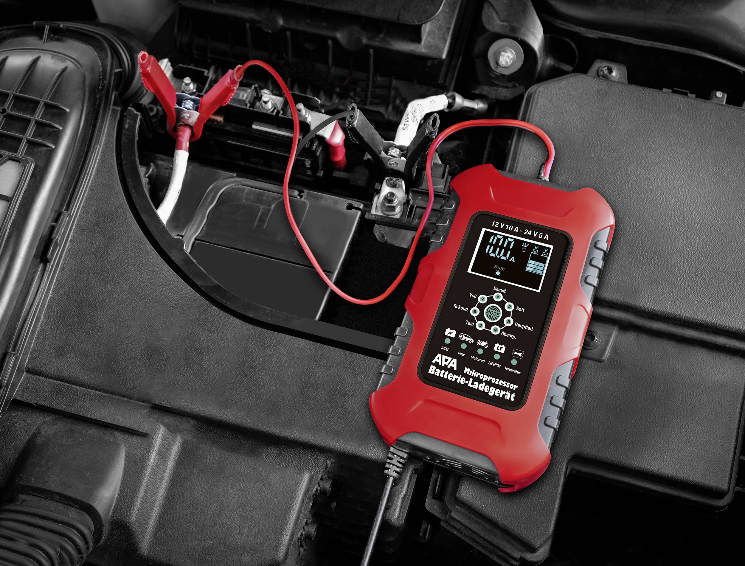 Red battery charger, connected to a car battery. Device displays charging information on the screen.