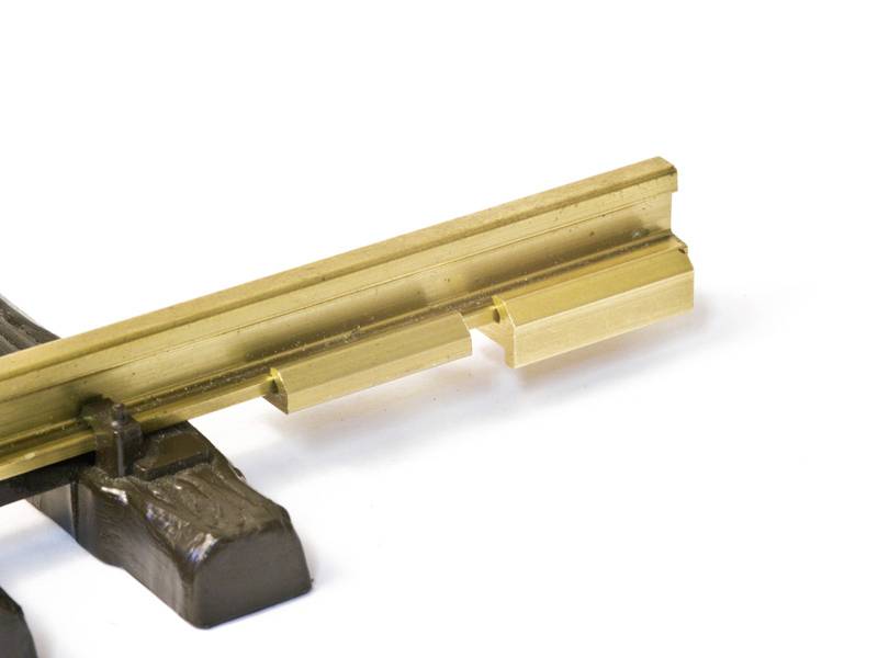 A golden metal component resting on a brown stand, potentially representing a model of a workpiece or a rail.