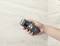 A hand is holding a digital moisture metre against a bright, tiled wall. The display shows '12%'.