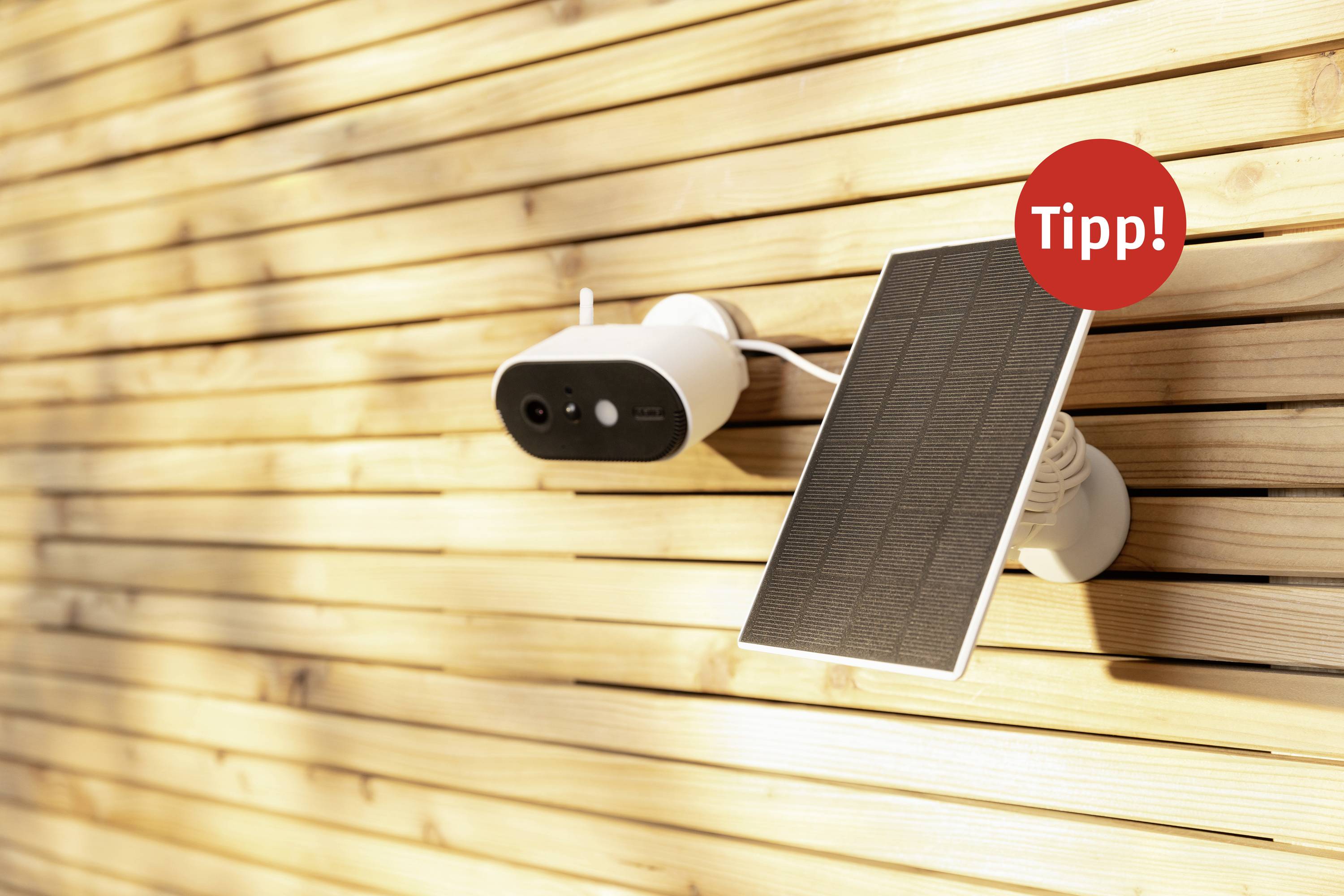 Security camera with solar panel on a wooden wall. A red circle with the word 'Tip!' highlights a key point.