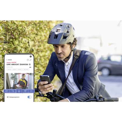 Man in suit and helmet looking at his smartphone next to bicycle. A live surveillance camera feed is displayed on the mobile phone screen.