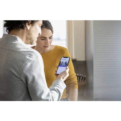 Two people are examining a smartphone. The woman is wearing a yellow jumper, and the man has on a grey top. They appear focused.