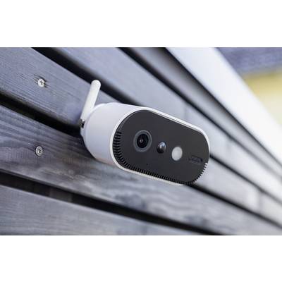 A surveillance camera is mounted on a wall. It has a white antenna and a black front panel with a lens and sensors.