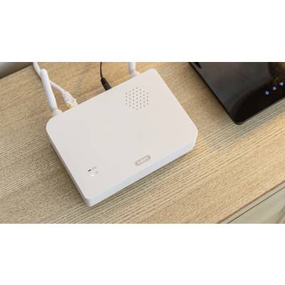 A white Wi-Fi router with two antennae sits on a wooden table. Next to it is a black device.
