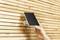 A hand is attaching a small solar panel to a light brown, vertically striped wooden surface.