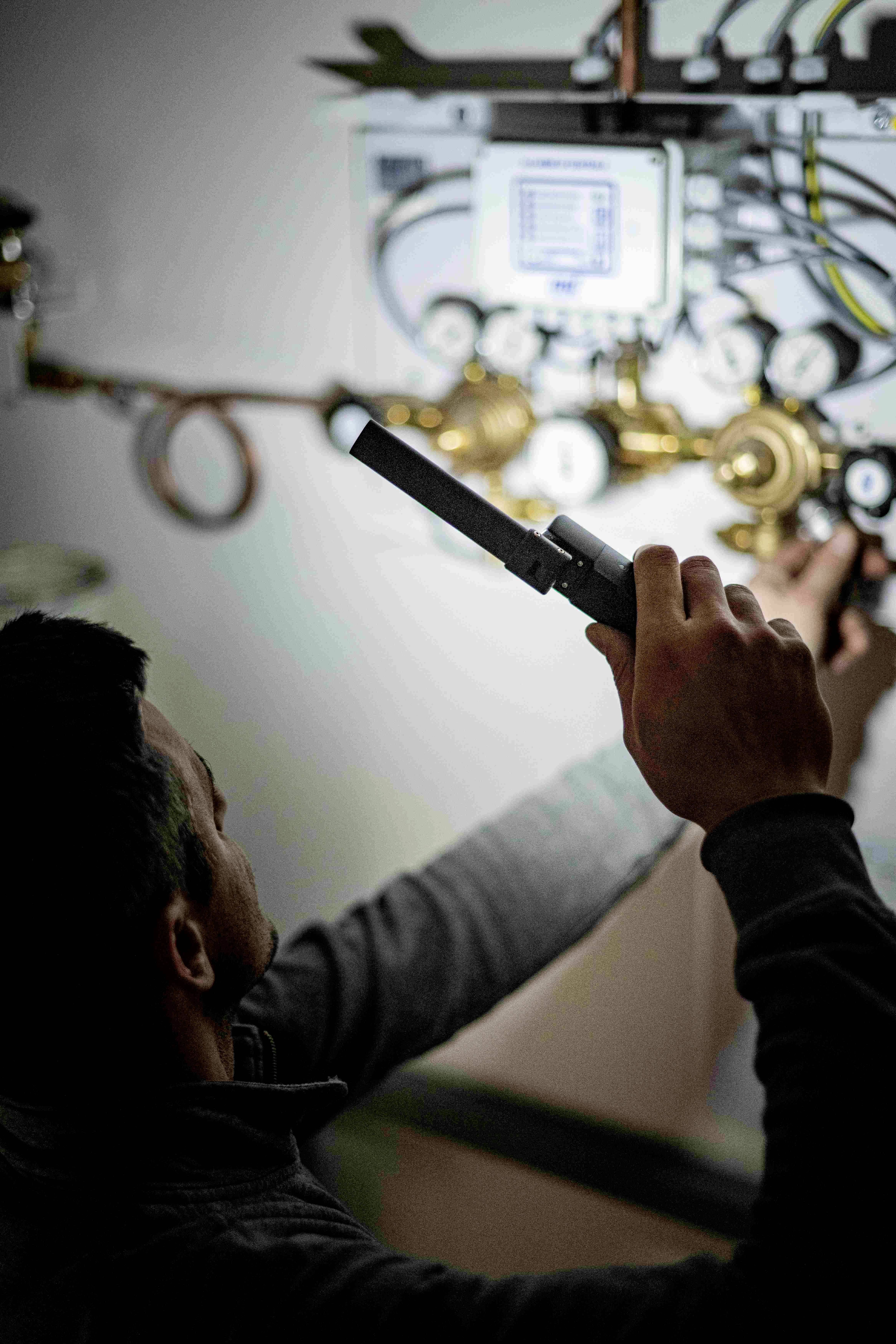 A technician repairs a complex piping system with tools, surrounded by gauges and controls.
