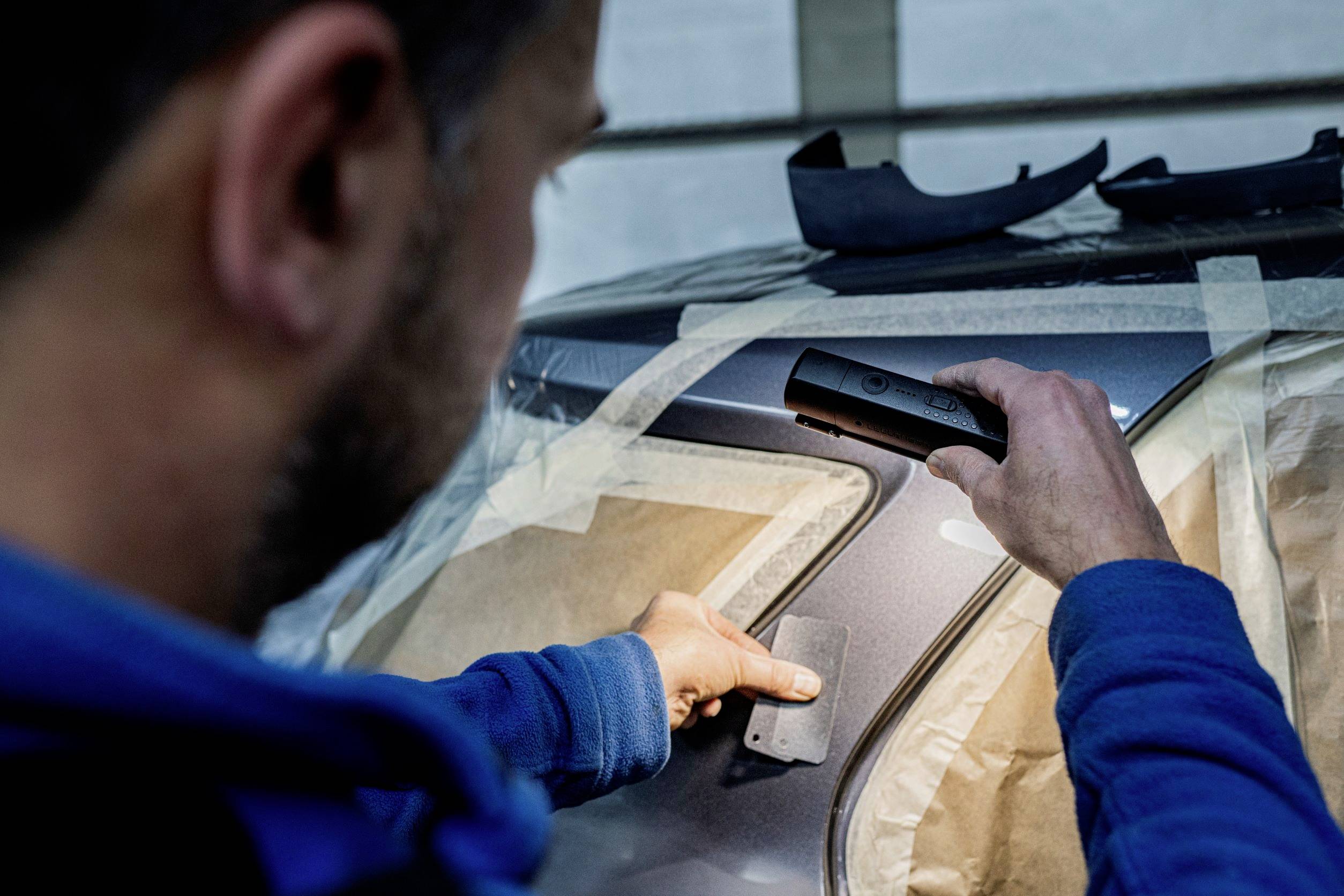 A man is repairing or inspecting a scratch on a car, using a specialised tool.