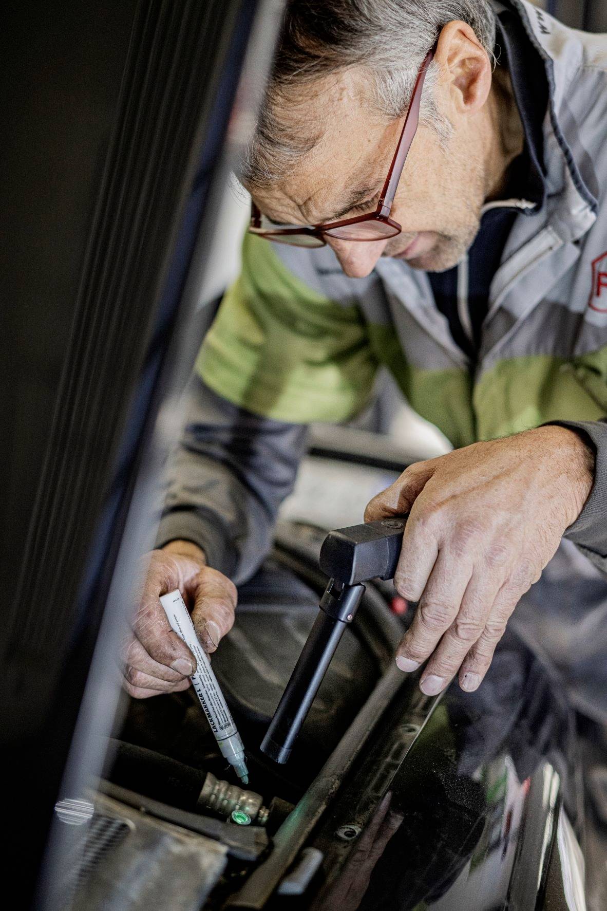 A mechanic is inspecting a car with an inspection lamp and checking something with a pen.