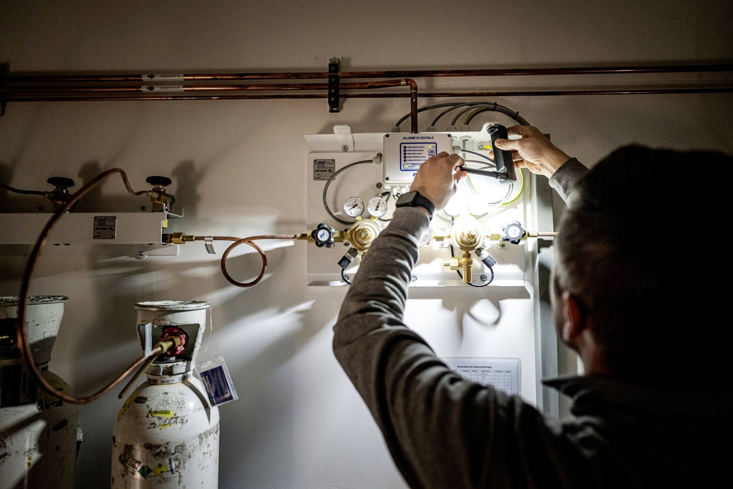 A person is working on a gas pressure regulation system, adjusting valves and checking indicators. Gas cylinders are visible in the background.