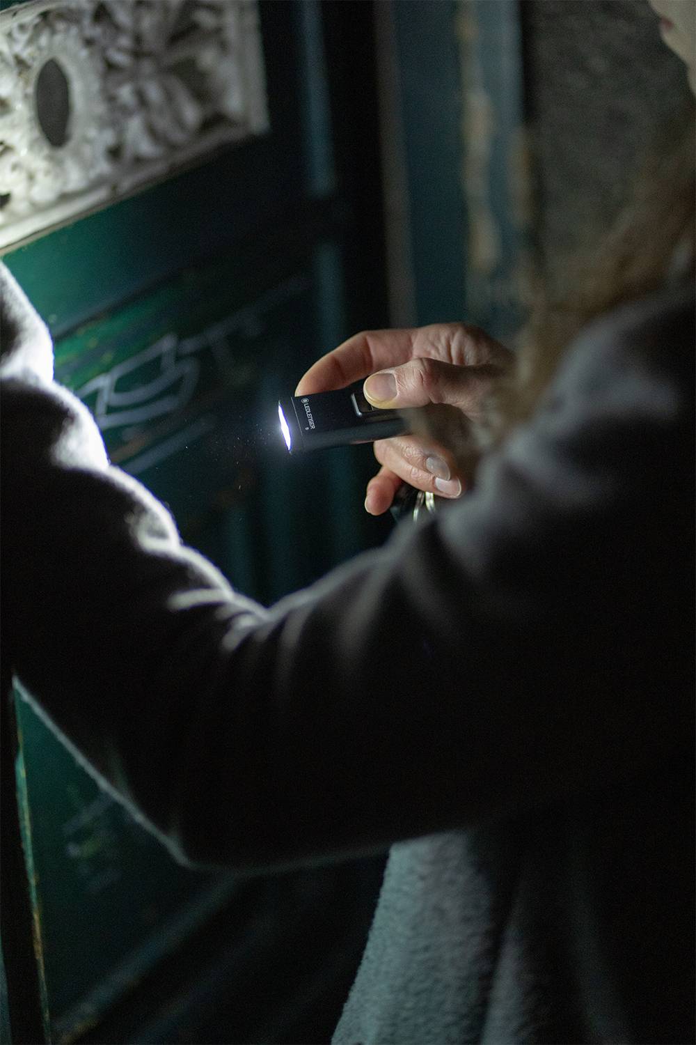 A person is holding a small torch and shining it on a green door to illuminate it in the dark.