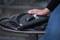 A hand is holding a bunch of keys with a torch on a black bag resting on a bench.