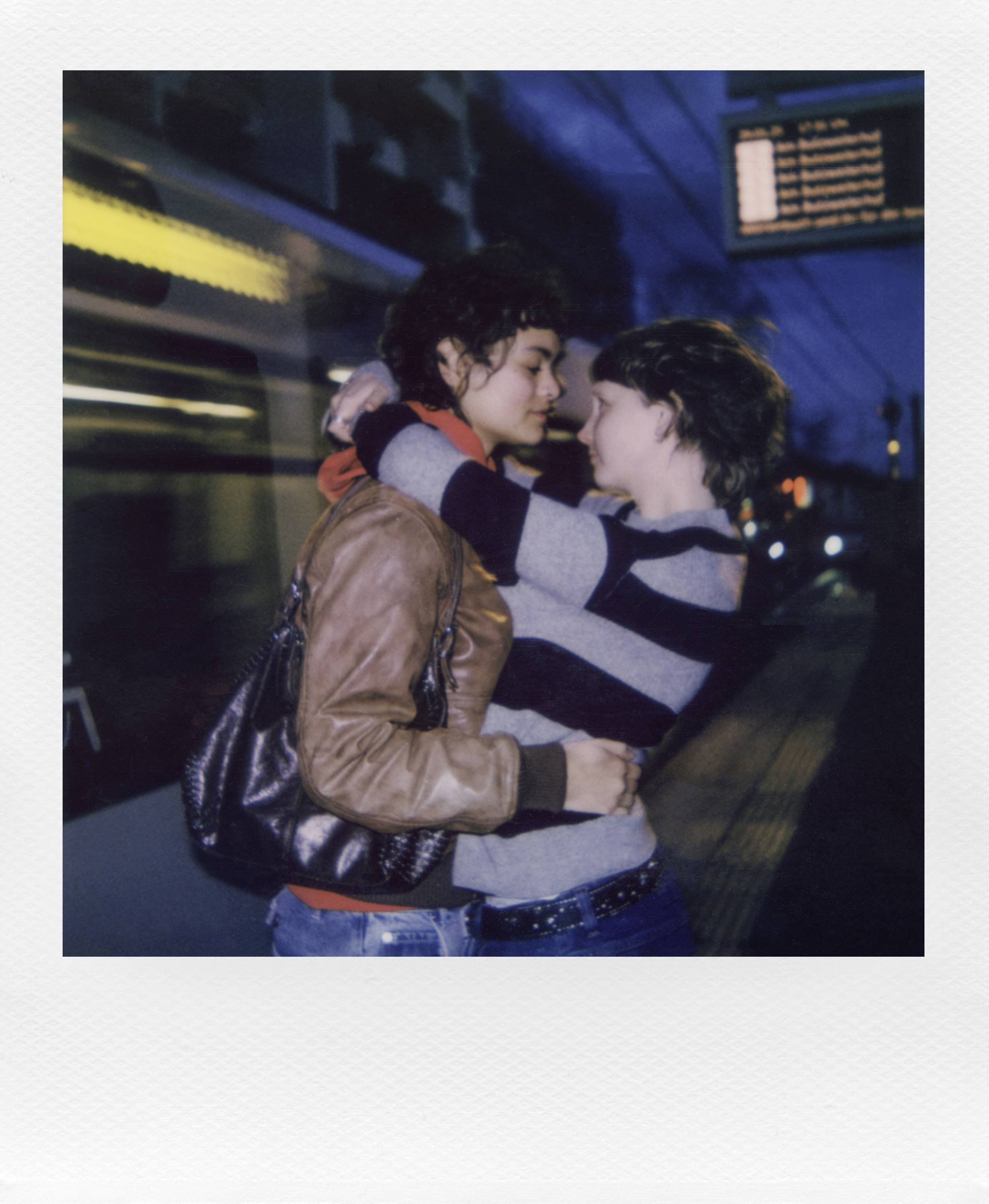 Two people embrace on a platform at night, as a train passes by in the background.