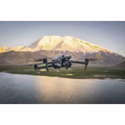 A drone is flying over a lake, with snow-capped mountains visible in the background. The drone has green and red lights.