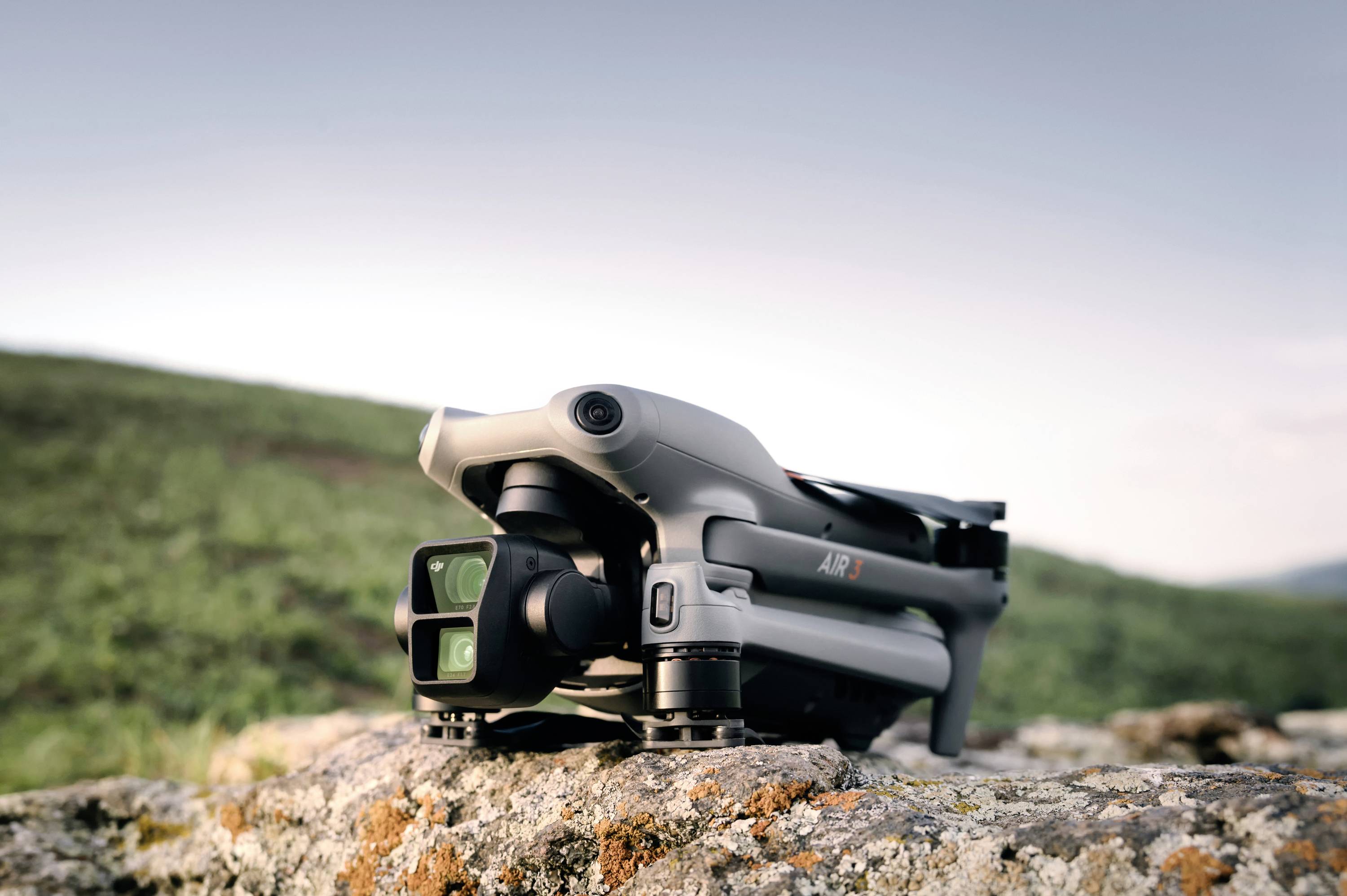 A grey drone lies on a rock in a natural setting. Blurred green landscape can be seen in the background.