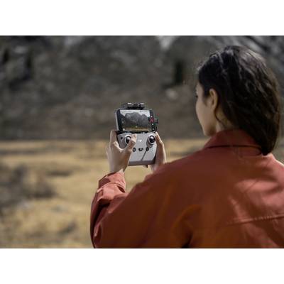 A person in a red jacket is filming a mountainous landscape panorama on a screen using a drone remote control.