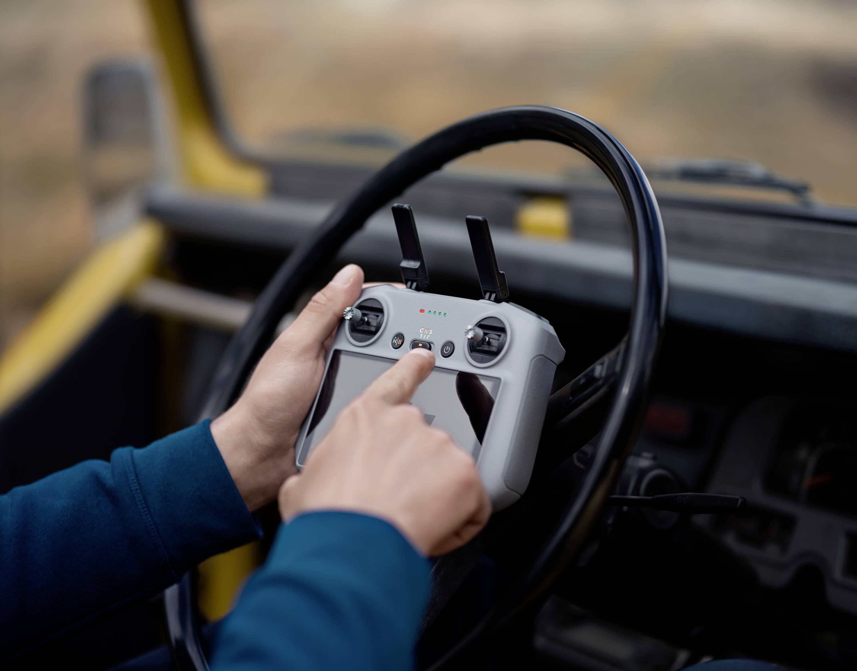 A person is controlling a device with a controller in a car, likely a drone or a vehicle. Hands are steering the equipment, with a focus on technology.