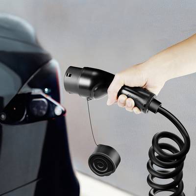 A hand is holding a spiral-shaped charging plug, ready to be plugged into an electric car.