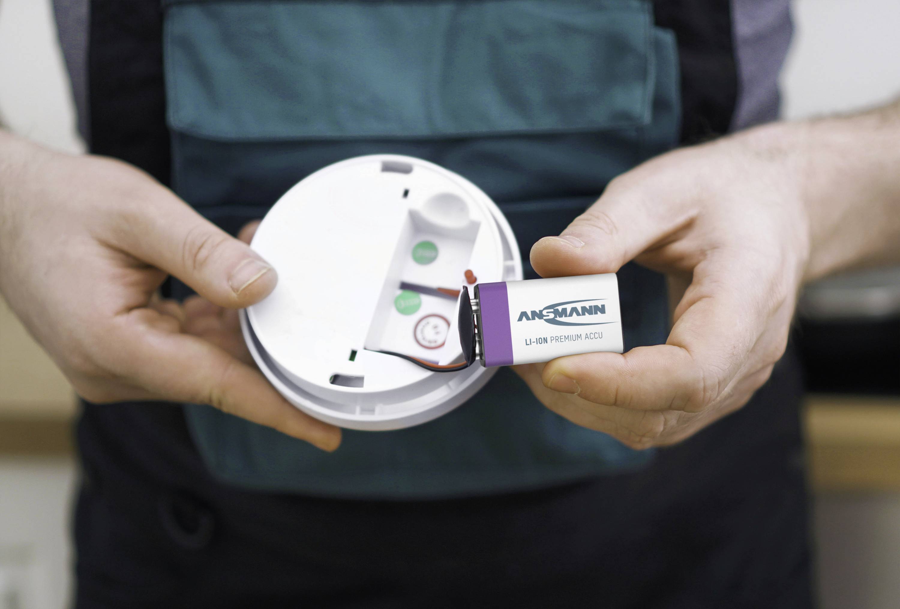 A person is installing a 9-volt battery into a smoke detector. The smoke detector is open, and the battery is visible.