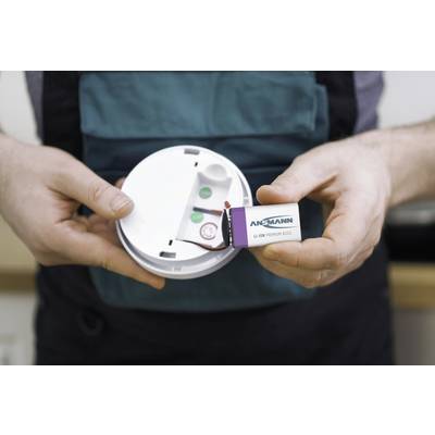 A person is installing a 9-volt battery into a smoke detector. The smoke detector is open, and the battery is visible.