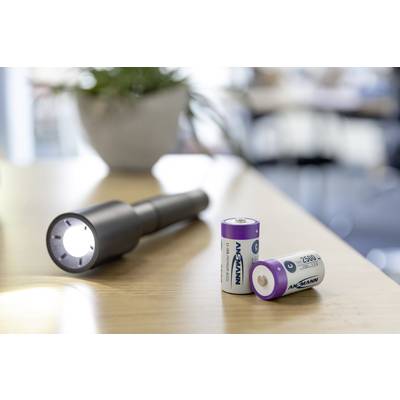 A torch illuminates a table. Two batteries are placed beside it. In the background, a blurry, bright room can be seen.