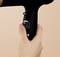 A hand is holding a black hairdryer. The controls on the handle show settings from 0 to 3.