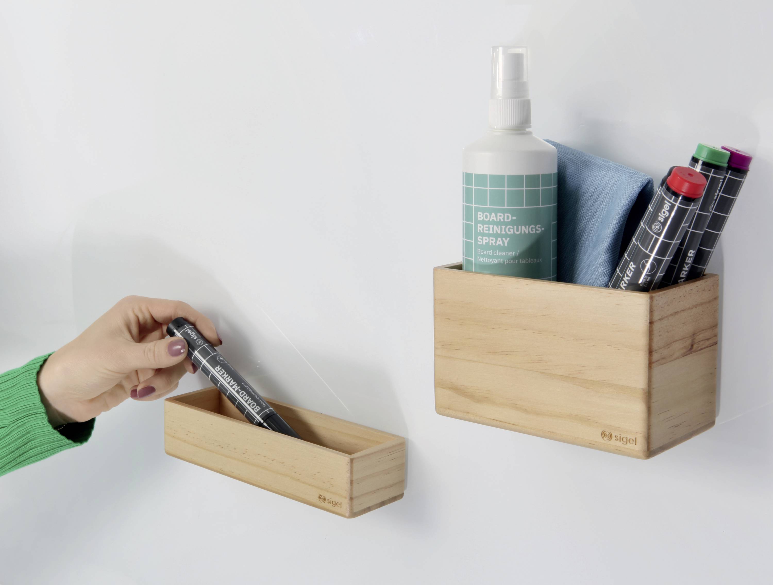 A hand takes a marker from a small wooden box. Beside it stands a larger box with cleaning products and additional markers.