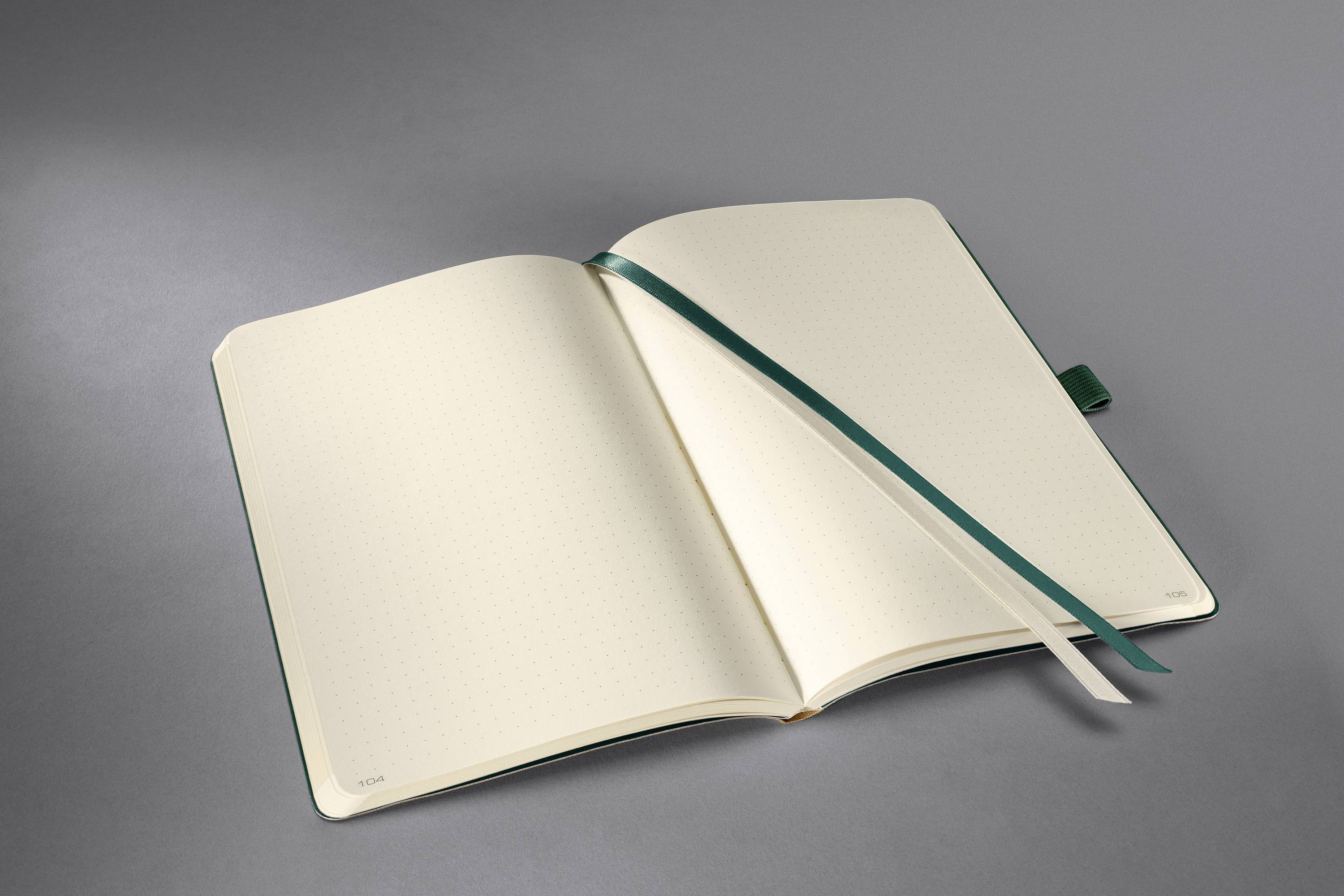 An open notebook with cream-coloured, blank pages and a green ribbon bookmark lies on a grey background.