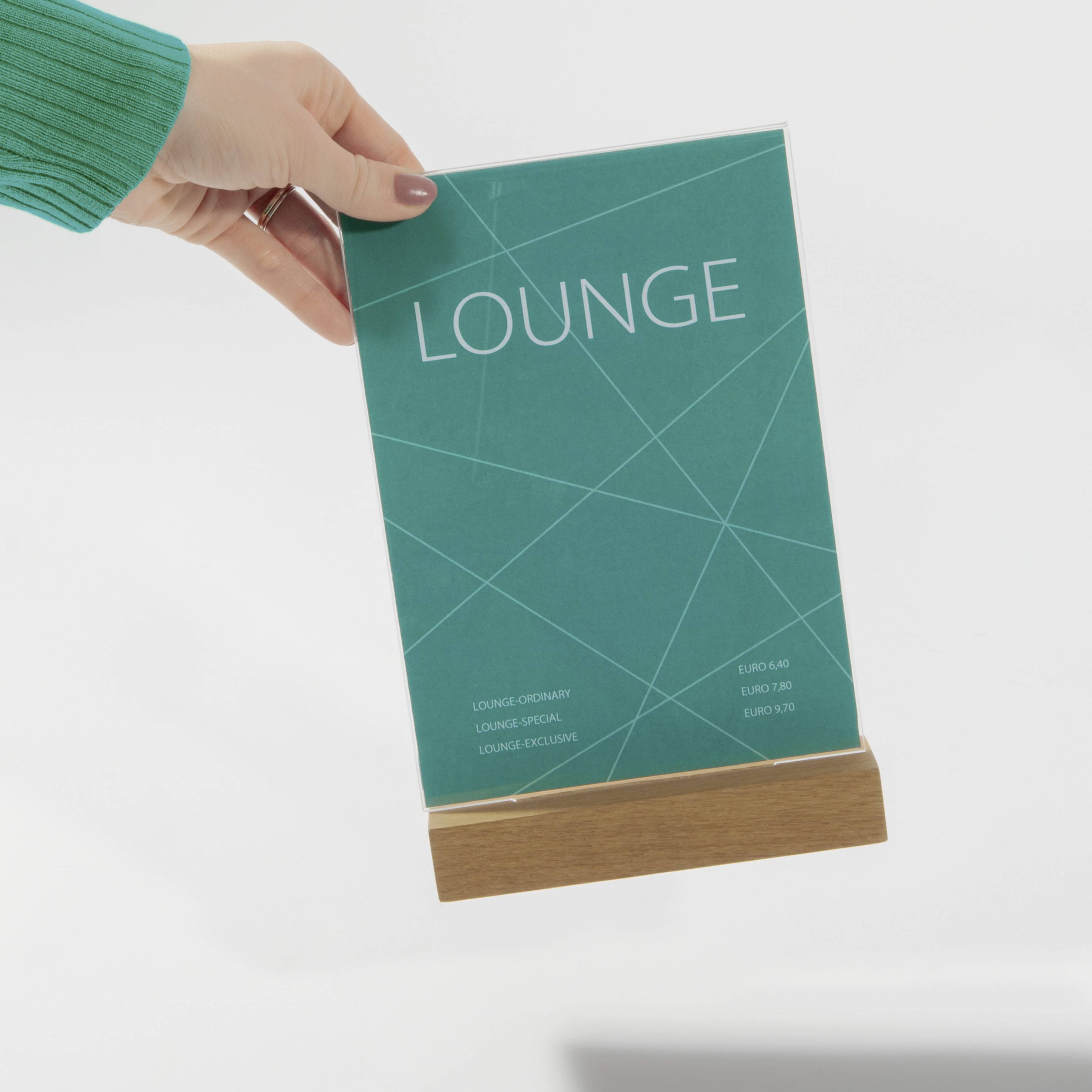 A hand is holding a green menu sign with the word 'Lounge' written in white text. The sign is placed on a small wooden stand.