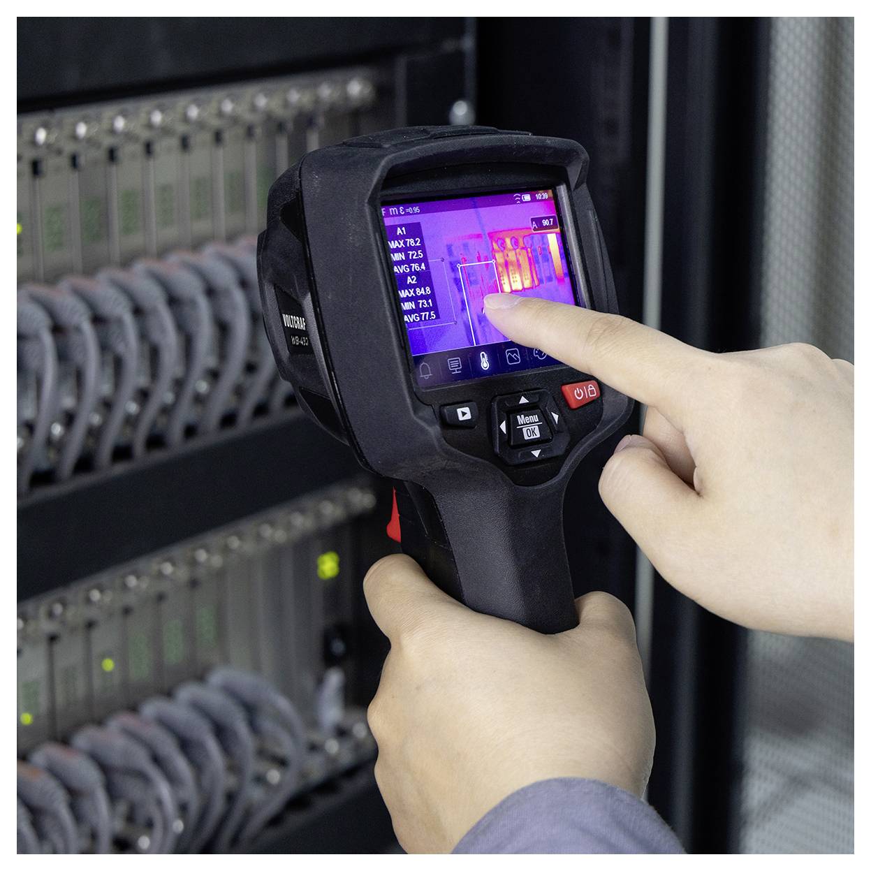 Person using a thermal imaging camera to inspect server rack equipment, with the screen showing heat patterns on electronics.<br>