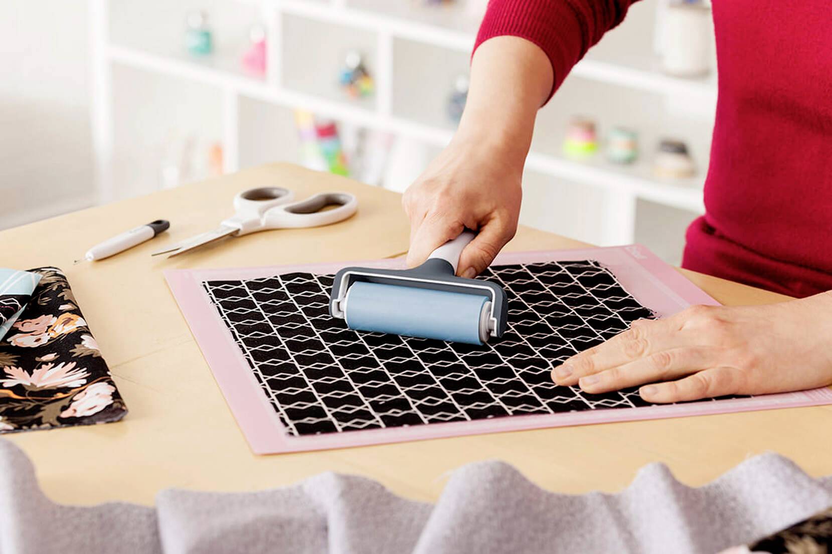 A person is using a blue roller on fabric with a geometric pattern on a table with scissors and tools.