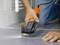 A person is repairing a tiled floor using an orange multi-functional electric tool. The tool is cutting through the grout.