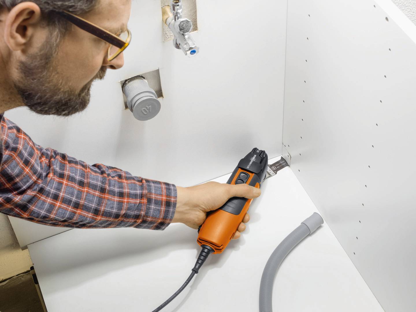 A man is using a testing device to check the water flow in a pipe beneath a sink.