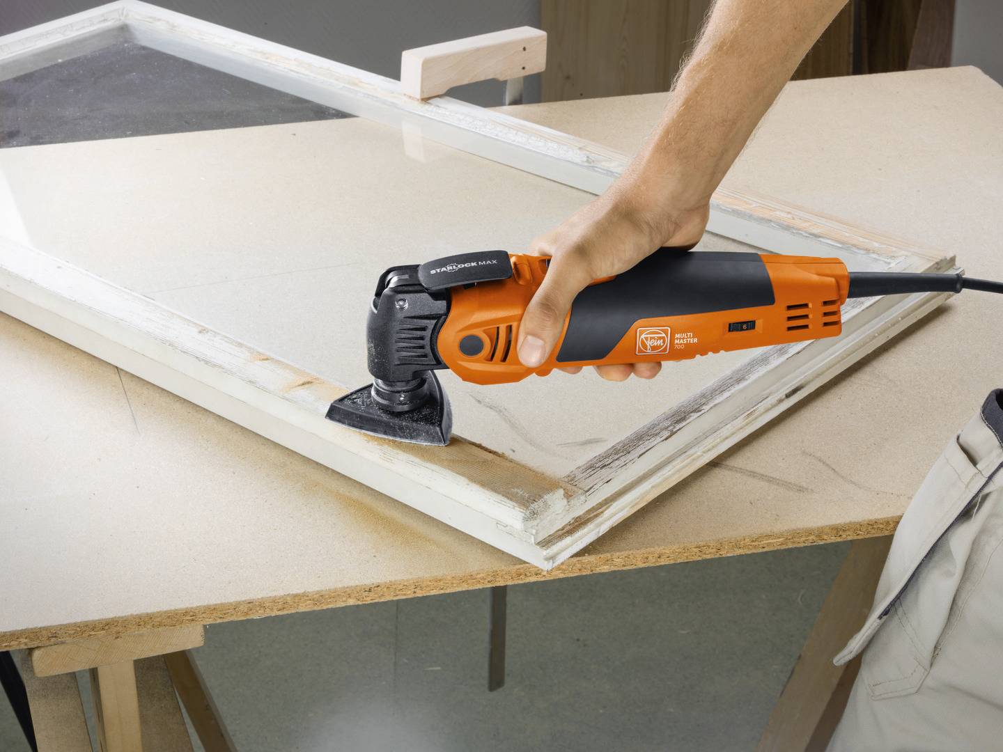 A person is using an oscillating multi-tool to sand paint off a window frame.