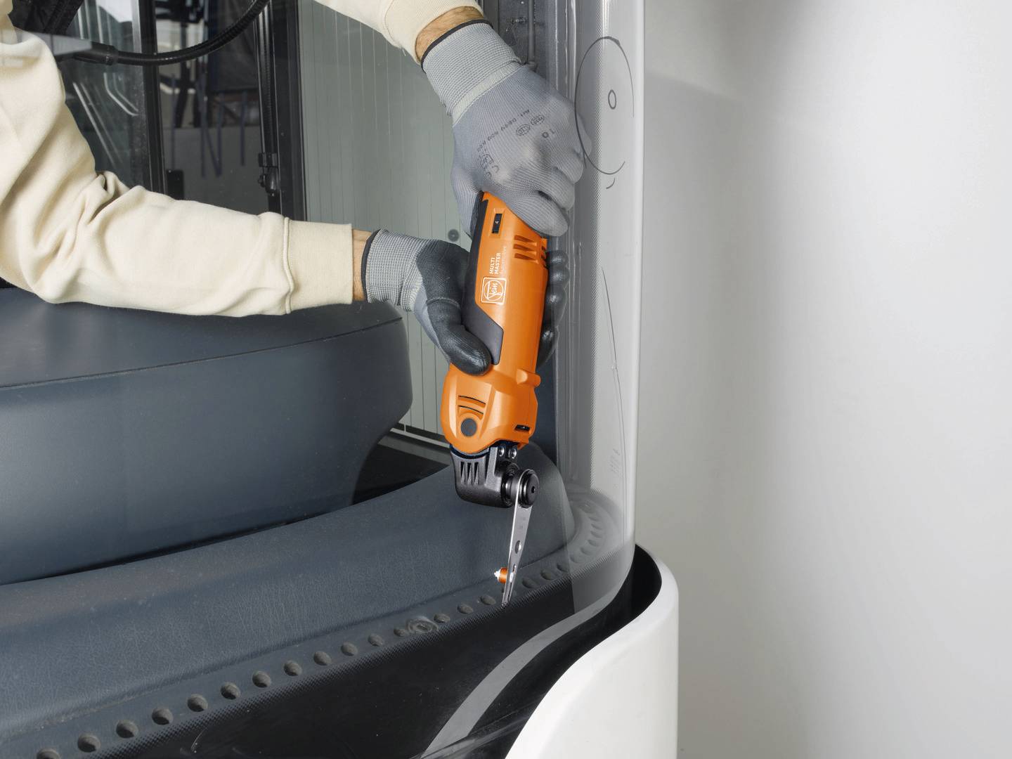 A person is cutting a piece of plastic with an orange electric tool. The person is wearing gloves.