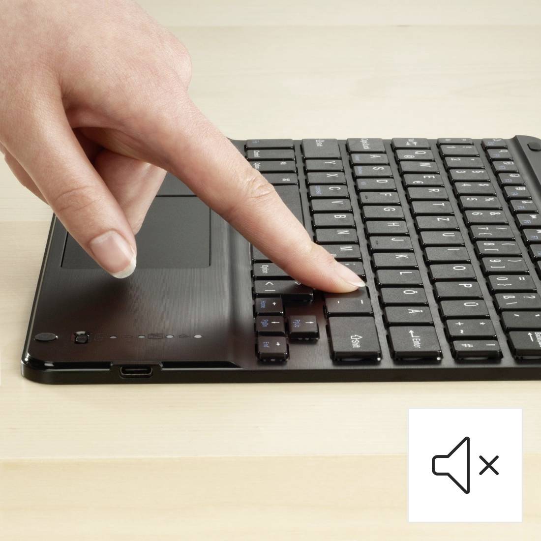 A hand is pressing a key on a laptop keyboard. A speaker symbol with an 'x' indicates that the sound is muted.