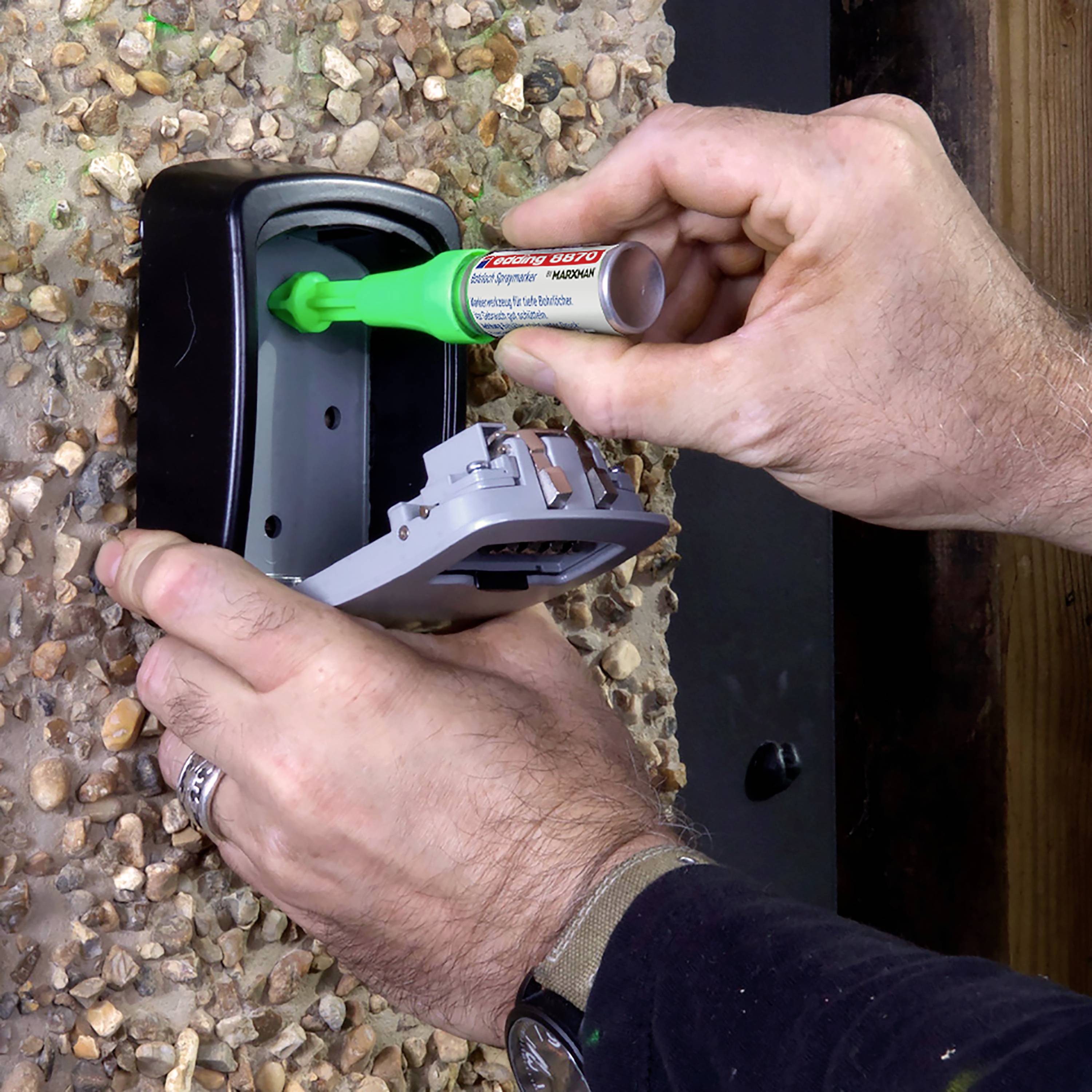 A person is filling adhesive into a dispenser mounted on the wall. The dispenser has an open flap.