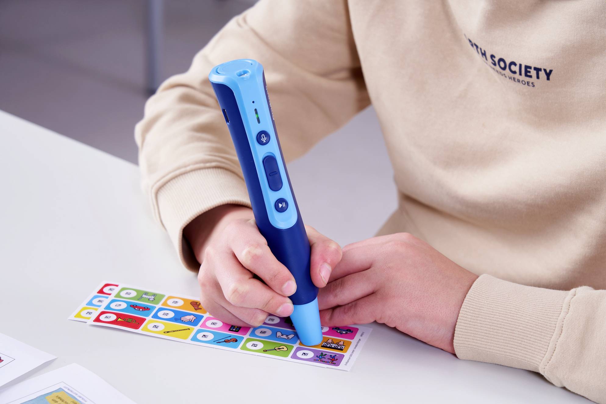 A person is holding a blue pen, pointing at colourful stickers printed with symbols. The focus is on an interaction with the pen.
