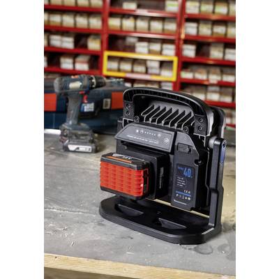 A workshop shot shows a battery-powered work light in the foreground, surrounded by shelves with parts. In the background is a drill.