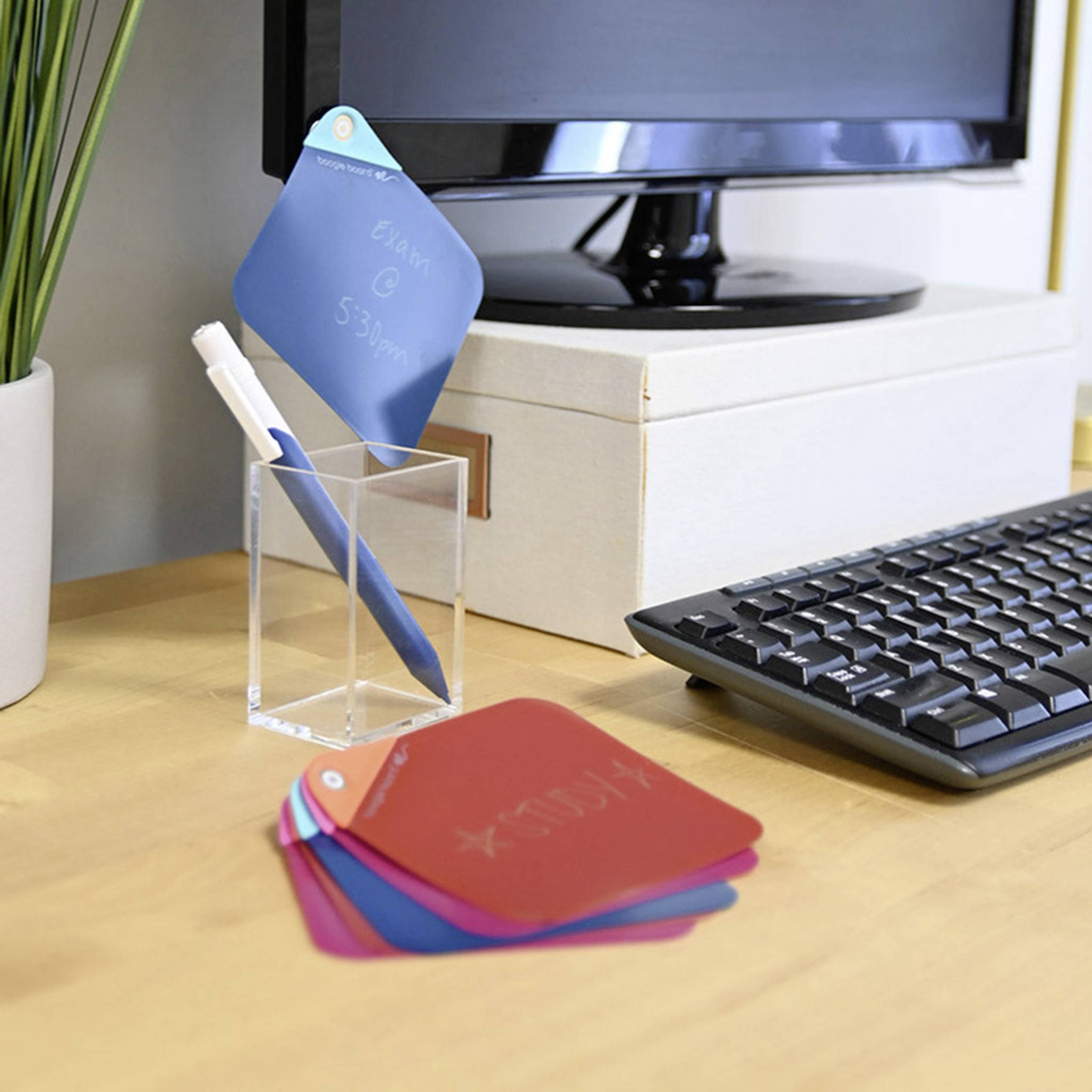 A desk with a monitor, keyboard, computer tower and a pen holder with writable cards that can be used for notes.